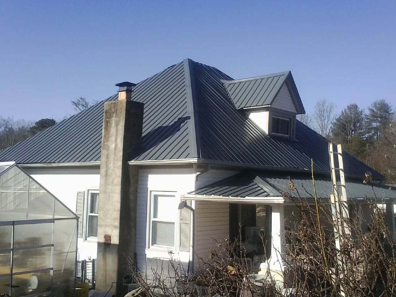 Dark blue standing seam metal roof on a white farmhouse with dormer — Slate & Tile Roof Repair by Roofing Brothers in East Schodack