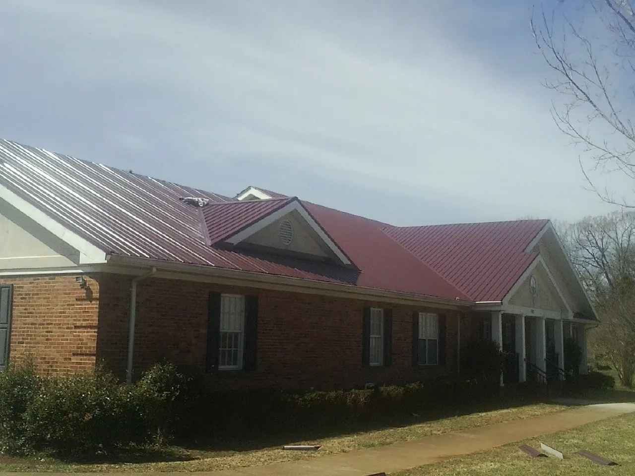 Red metal roof with gabled entries on a long brick building, from a Hail Damage Roof Repair job in East Schodack