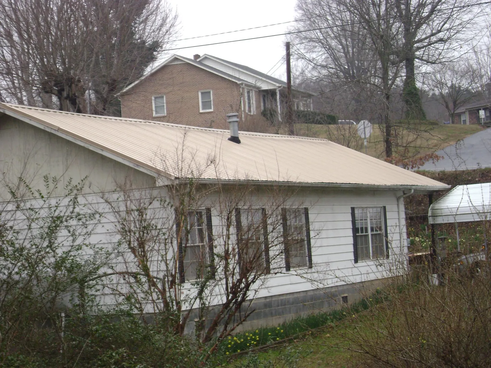 Tan metal roof on a white sided house set into a hillside — Commercial Roofing by Roofing Brothers in East Schodack